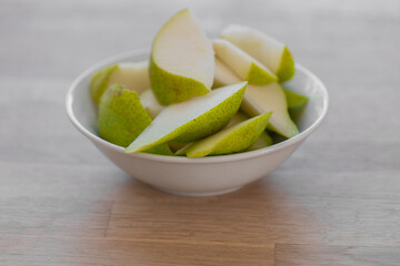 Sliced pear.cutting green pear into a plate on a wooden table in a bright kitchen.Fruit cut....