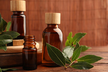 Bottles of bay essential oil and fresh leaves on wooden table