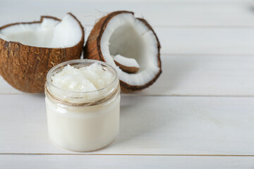 Jar of organic coconut cooking oil and fresh fruits on white wooden table, space for text