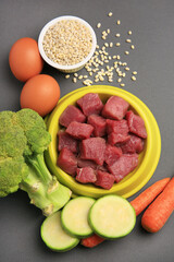 Raw meat in bowl and healthy products for pet on black background, flat lay