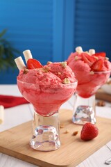 Delicious scoops of strawberry ice cream with wafer sticks and nuts in glass dessert bowls served on white table