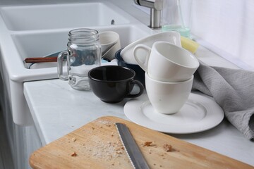 Many dirty utensils and dishware on countertop in messy kitchen