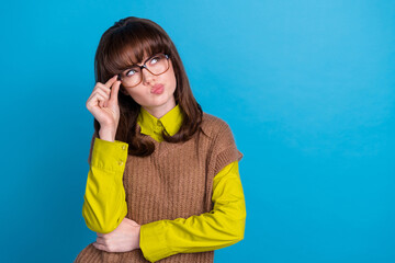 Photo of minded woman with vintage hair dressed knitwear jumper touch eyewear squinting look empty space isolated on blue color background