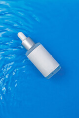 Facial essence bottle mockup. Serum to moisturize the skin. The bottle lies on a blue background in the waves. A daily treat for healthy skin. Anti edge cosmetics