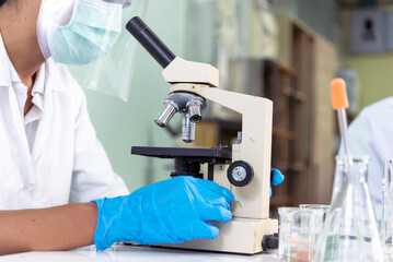 Scientist man look into Microscope research in science laboratory. Asian scientist looking equipment laboratory chemistry labs. Covid-19 coronavirus biochemistry research experiment vaccine concept