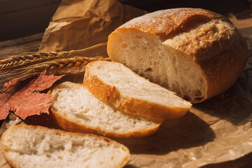 Sliced fresh loaf of bread in paper packaging with ears of wheat and maple leaves on a wooden table.