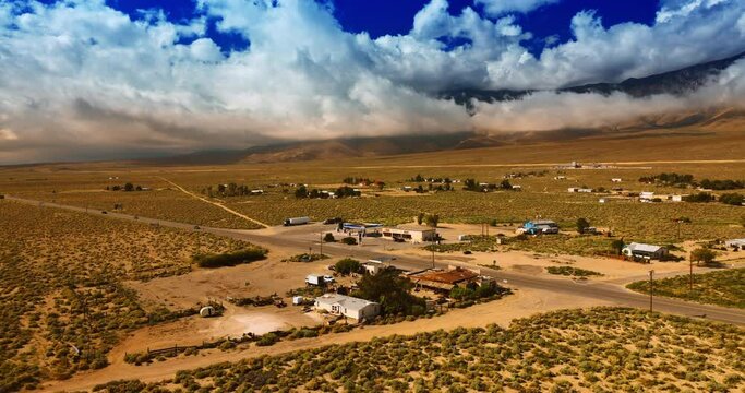 Approaching the village in the desert of Death Valley, California. Some households are scattered in the area around the highway. Mountains hidden by clouds at backdrop.