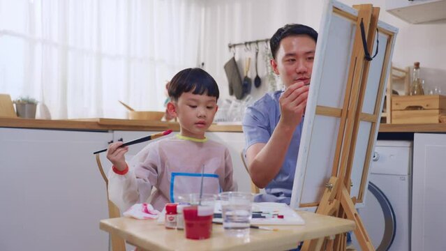 Adorable Asian young son drawing picture on paper with parent in house. 