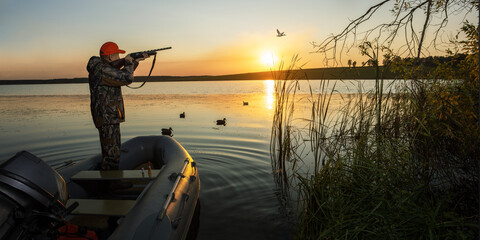 waterfowl hunter shooting into flying duck during duck hunting at sunrise or sunset. bunner with...