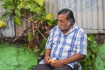 Old latino man, tired gentleman thinking about life sitting in a chair next to plants
