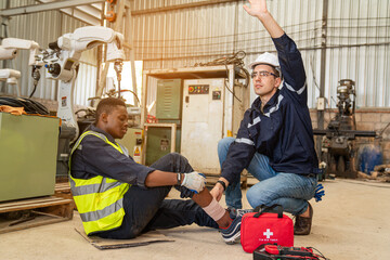 Fototapeta na wymiar Mature foreman in workwear giving first aid to staff suffering after working injury in industrial factory, Injury at work.