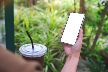 Mockup image of a woman holding mobile phone with blank white desktop screen while drinking coffee in the garden