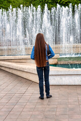 woman  with very  long hair standing in front of a water fountain jet in an urban setting