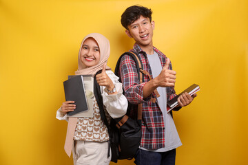 Cheerful Asian muslim students in casual clothes holding books and carrying backpack, showing...