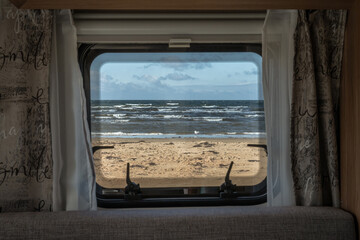 Ocean beach Sea view from the window of a camping caravan camper trailer. Road trip on the coast of...