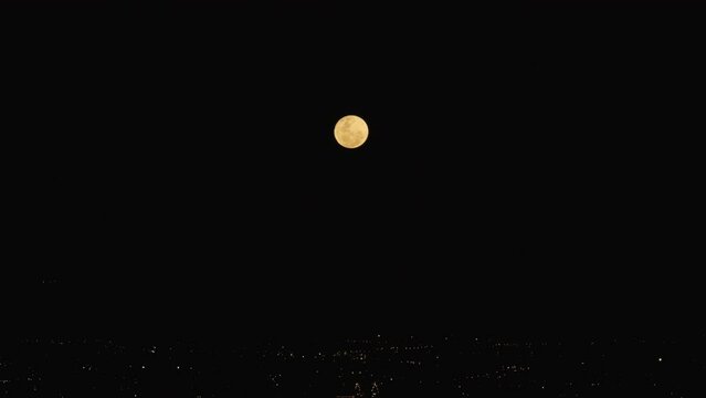 Time lapse of the full moon at the night rising over city lights
