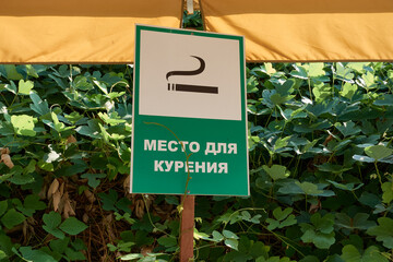 Indoor smoking sign against foliage background. The inscription on the sign - Smoking area.
