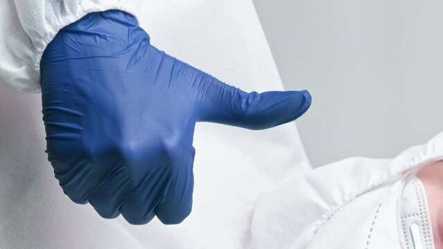 Vertical video. Successful treatment. Like gesture. Healthcare doctor specialist in white medical suit mask with blue glove hand thumb up sign.