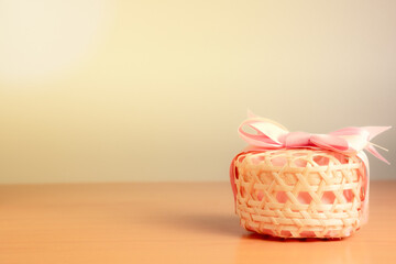 A woven wooden basket with a pink bow-tied lid placed on the right side of the warm, white background