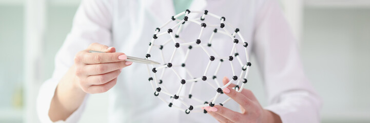 Woman scientist shows model of molecular structure in her hands, sitting at laboratory table.