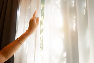Foto op Plexiglas A woman's hand opens the white curtains on the window in the bedroom. In the morning, she looked at the view of the mountains and trees. admire nature along with freshness © Photo Sesaon