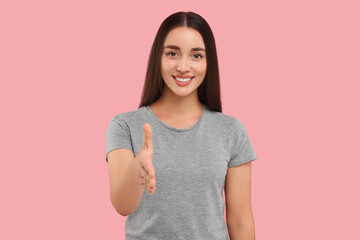 Fototapeta premium Happy young woman welcoming and offering handshake on pink background