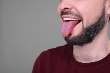 Fototapeta premium Happy man showing his tongue on light grey background, closeup. Space for text