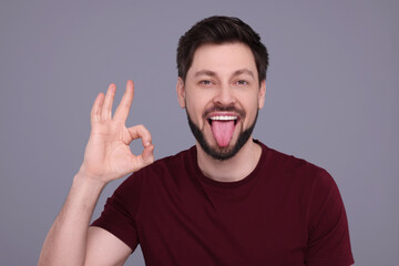 Happy man showing his tongue and making ok gesture on light grey background