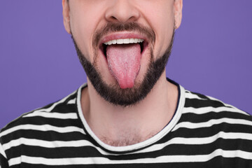Obraz premium Happy man showing his tongue on purple background, closeup