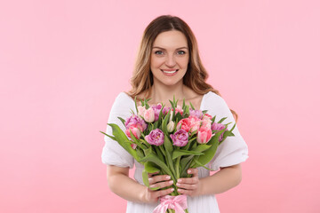 Happy young woman with bouquet of beautiful tulips on pink background