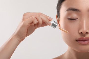 Beautiful young woman applying cosmetic serum onto her face on white background, closeup