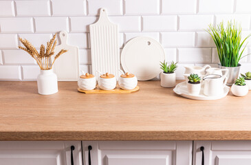 White kitchen utensils, cutting ceramic boards and dishes, a vase with ears of corn in the interior of a modern kitchen in white tones.