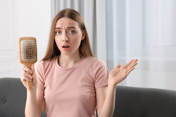Emotional woman holding brush with lost hair at home. Alopecia problem