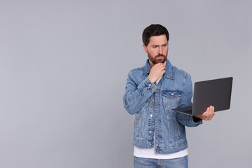 Confused man with laptop on light grey background. Space for text