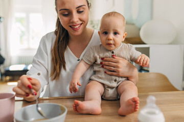 Happy mother is feeding her baby with homemade baby porridge.