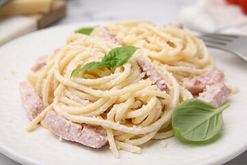 Tasty pasta Carbonara with basil leaves on plate, closeup