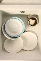 Clean tableware in white sink, top view