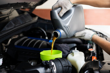 Pour car lubricant from a gray bottle on the background of the engine. Oil change service, auto...