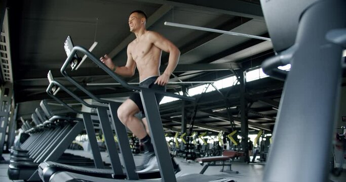 Athletic man exercising at gym and running on treadmill. Shirtless young male with muscular body has cardio workout at sport club. Healthy lifestyle concept.