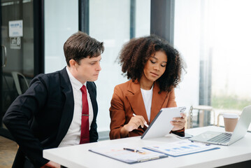 Businesswomen work and discuss their business plans. A Human employee explains and shows her colleague the results paper in modern office.