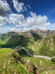 Beautiful landscape with mountains and peaks in the snow and a valley with roads and a lake on a summer sunny day with blue skies and clouds. View of the valley in Adjara, Georgia