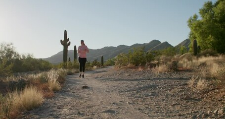 Fit millennial woman jogging through desert path with cactus while sunset