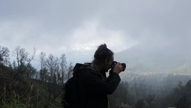 Caucasian backpacker man taking photo in foggy smoke forest mountain