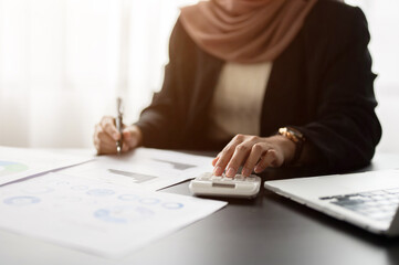 A professional Muslim or Arab businesswoman is analyzing business financial data on reports.