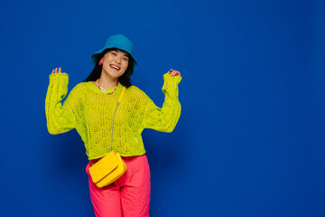 Cheerful asian woman posing while standing isolated over blue wall
