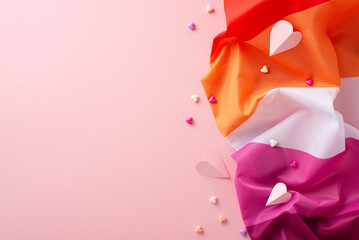A top-down shot of the Lesbian Pride flag alongside tiny hearts expressing affection, on a soft pastel pink backdrop with space for text or ads