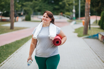 Happiness fills the air as an overweight woman takes a post workout break outdoors. She smiles with...