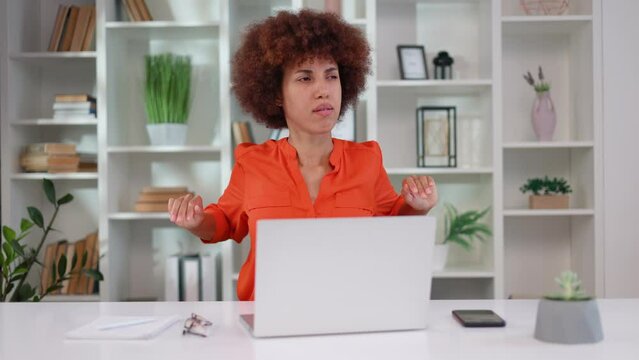 Multiethnic dark haired woman feeling discomfort during sudden pain in back while sitting at modern office. Tired young lady wearing orange blouse doing some exercises to relieve ache.