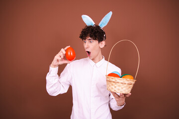 Young attractive man posing in an Easter bunny costume. Brown background.