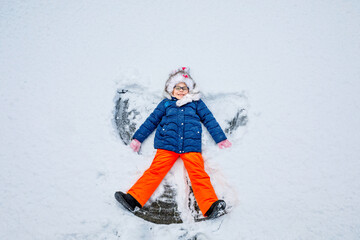 Fototapeta na wymiar Happy child girl playing on a winter walk in nature. Kid making snow angel. Happy preschool girl having fun on snowing winter day.